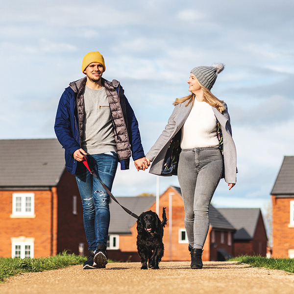 Happy couple walking the dog on a sunny autumn day - Young couple with a black dog on leash enjoying neighbourhood walk - Lifestyle and animals concepts