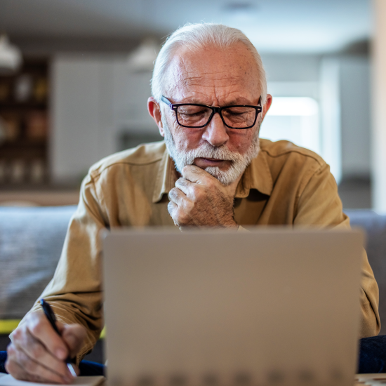 Older man using a laptop and making notes with a pen